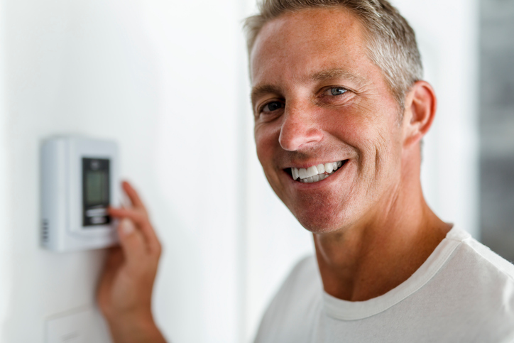 A Smiling Man Adjusting Thermostat On Home Heating System