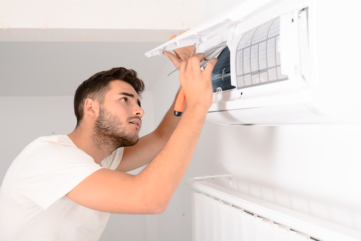 young man electrician installer working and cleaning air filter on a indoor unit air conditioner at client's home
