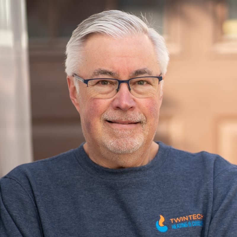 Professional portrait of a friendly Twintech HVAC technician wearing a branded blue sweater and glasses.