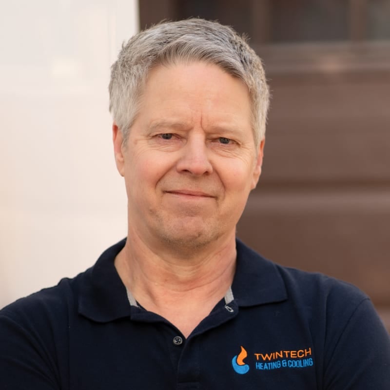 Professional portrait of Greg Dainty standing with arms crossed.