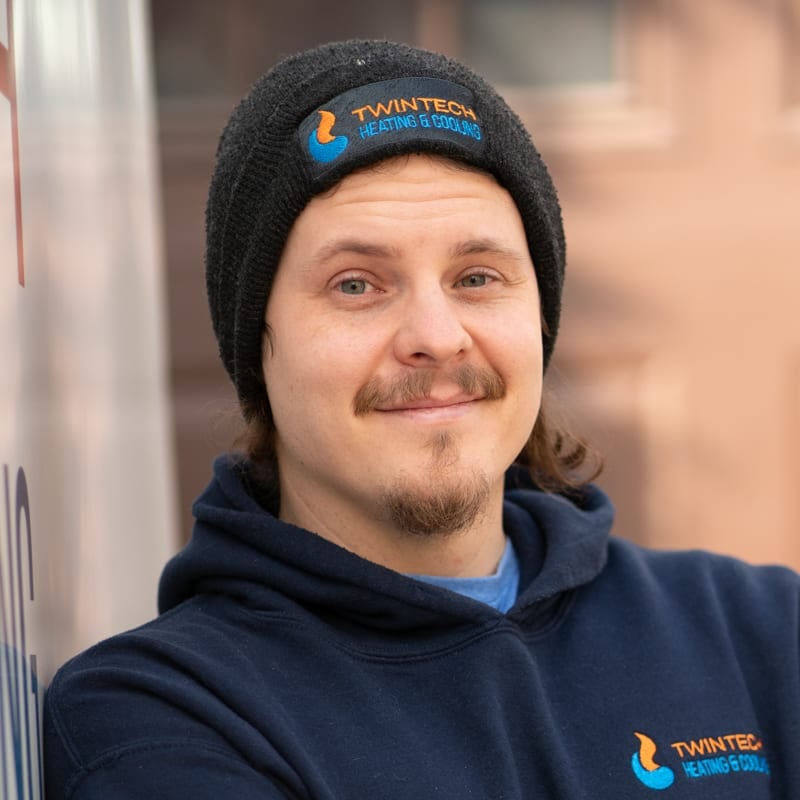 Professional Twintech HVAC technician in branded beanie and hoodie smiling outdoors.